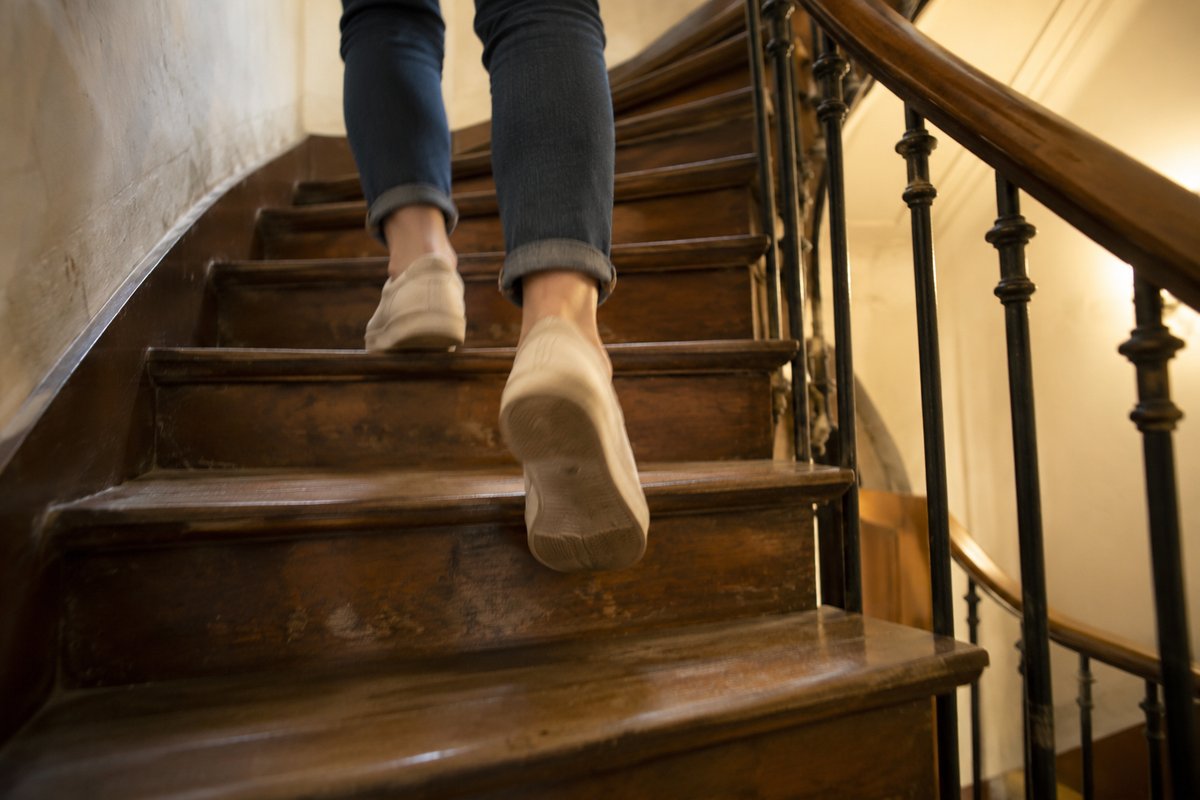 Des pieds en baskets montent l’escalier en bois d’un vieil immeuble